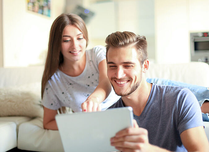 Ein junges Paar schaut sich gemeinsam etwas auf einem Tablet an.